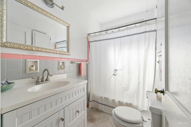 bathroom featuring a wainscoted wall, toilet, vanity, and tile walls