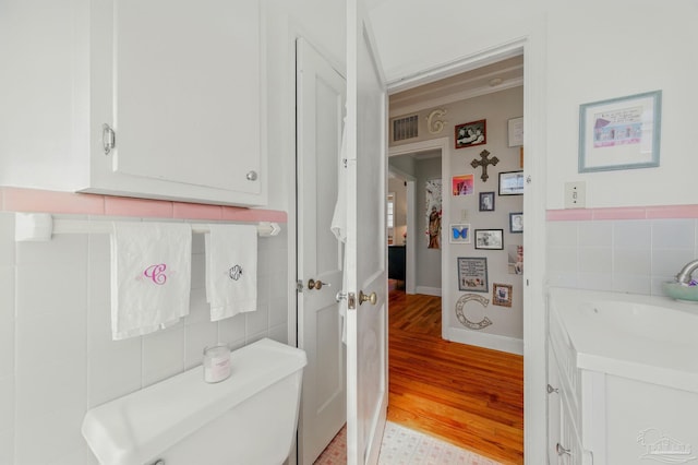 half bath with wood finished floors, vanity, tile walls, and visible vents
