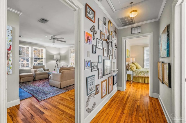 hallway with crown molding, visible vents, attic access, and hardwood / wood-style floors
