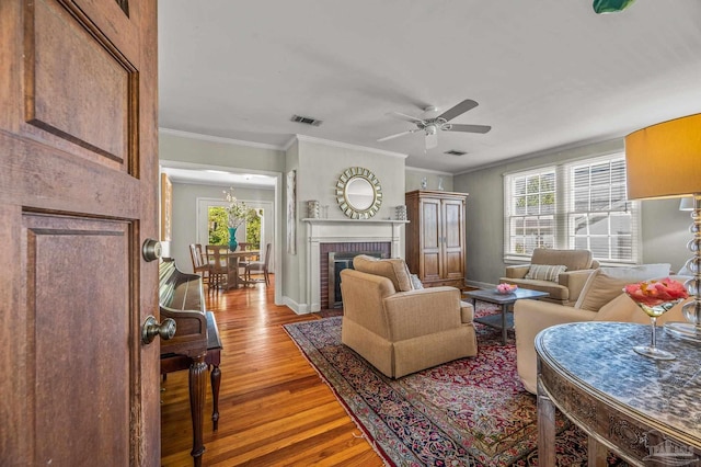 living area featuring a ceiling fan, wood finished floors, ornamental molding, and visible vents