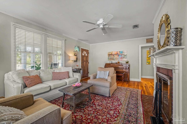 living area featuring a brick fireplace, visible vents, ornamental molding, and a ceiling fan