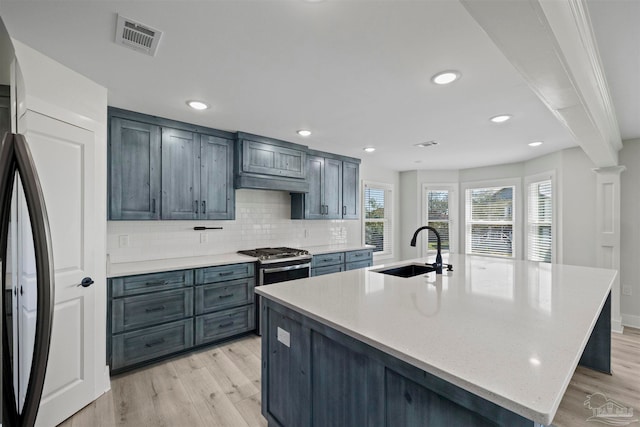 kitchen with a kitchen island with sink, sink, light stone countertops, appliances with stainless steel finishes, and light hardwood / wood-style floors