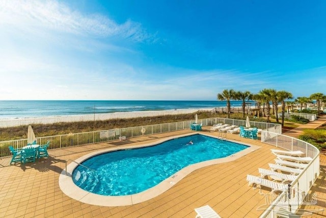 pool with a patio area, a water view, fence, and a view of the beach