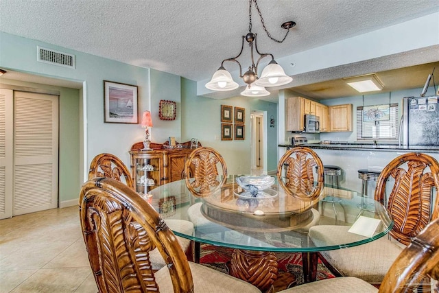 dining space featuring light tile patterned floors, visible vents, a textured ceiling, and an inviting chandelier