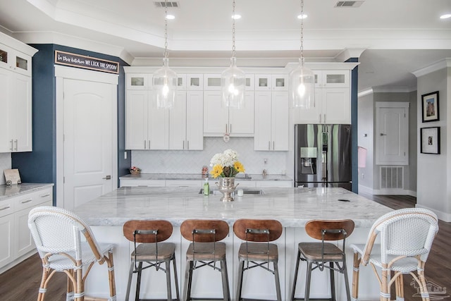 kitchen featuring dark hardwood / wood-style flooring, stainless steel fridge, light stone counters, and a large island with sink