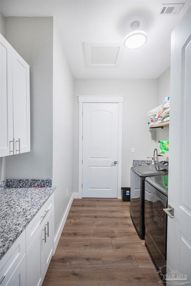 laundry area with washing machine and clothes dryer, hardwood / wood-style floors, and cabinets