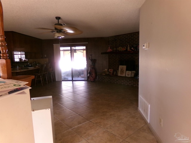 unfurnished living room featuring a brick fireplace, a textured ceiling, light tile patterned floors, and ceiling fan