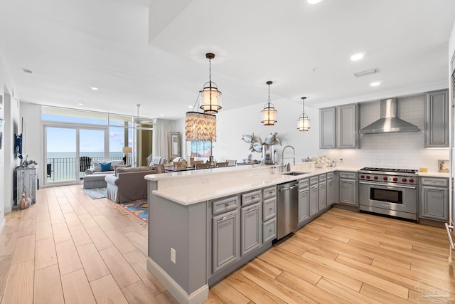 kitchen with appliances with stainless steel finishes, wall chimney exhaust hood, kitchen peninsula, and hanging light fixtures