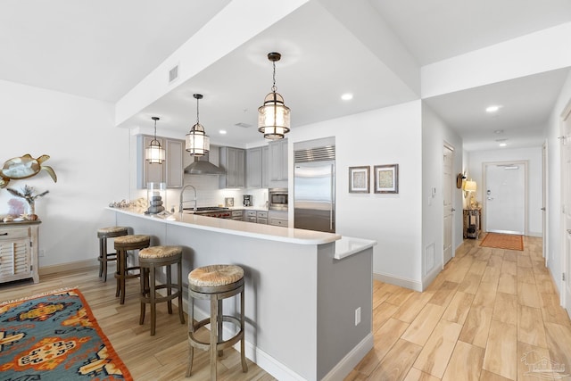 kitchen featuring gray cabinets, light hardwood / wood-style flooring, built in appliances, decorative light fixtures, and kitchen peninsula