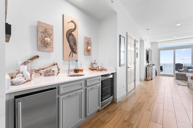 bar featuring sink, light hardwood / wood-style flooring, stainless steel fridge, gray cabinets, and beverage cooler