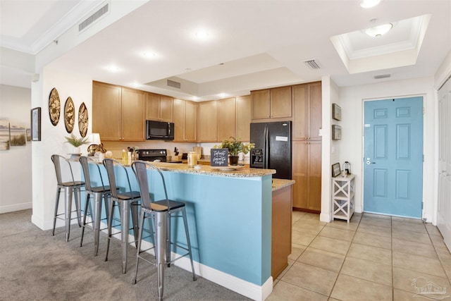 kitchen with a kitchen breakfast bar, black appliances, a raised ceiling, and kitchen peninsula