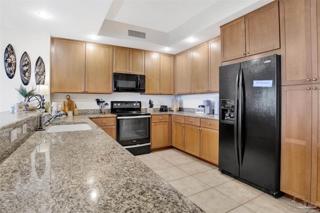 kitchen featuring sink, light stone counters, black appliances, light tile patterned flooring, and a raised ceiling