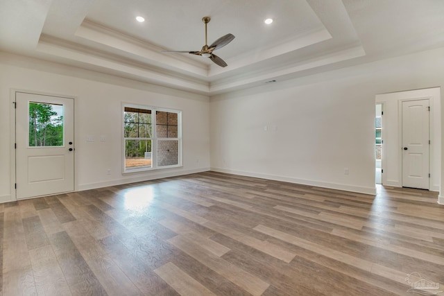 unfurnished living room with light wood-style floors, ceiling fan, baseboards, and a raised ceiling