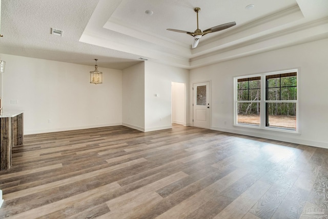 unfurnished living room with a ceiling fan, visible vents, a raised ceiling, and wood finished floors