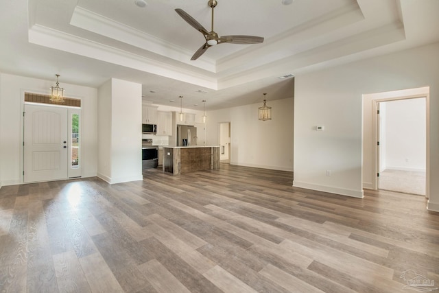 unfurnished living room with light wood finished floors, a tray ceiling, and a ceiling fan