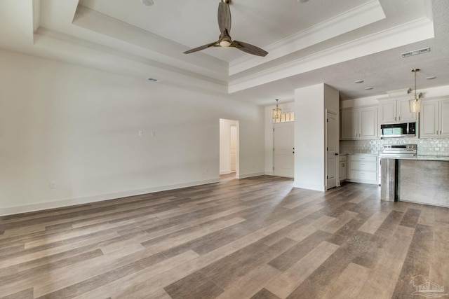 unfurnished living room with light wood-style floors, a tray ceiling, visible vents, and a ceiling fan