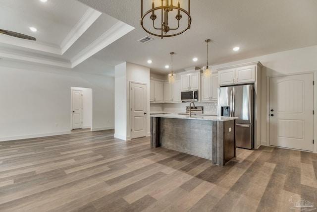 kitchen featuring a tray ceiling, light wood finished floors, stainless steel appliances, light countertops, and visible vents