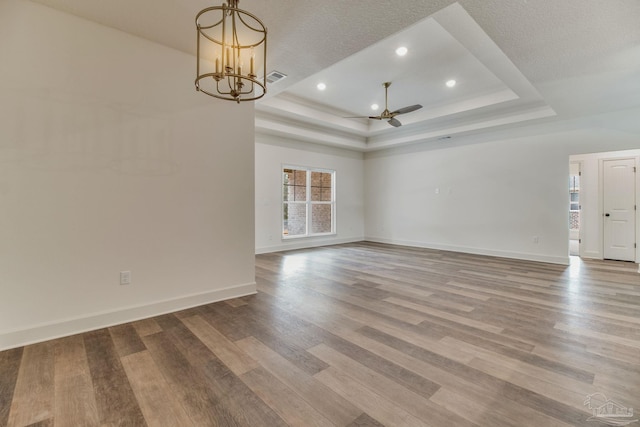 unfurnished room featuring baseboards, visible vents, wood finished floors, a tray ceiling, and ceiling fan with notable chandelier