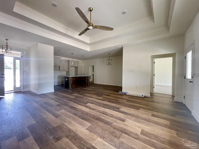 unfurnished living room featuring dark wood-style floors, a tray ceiling, ceiling fan with notable chandelier, and baseboards