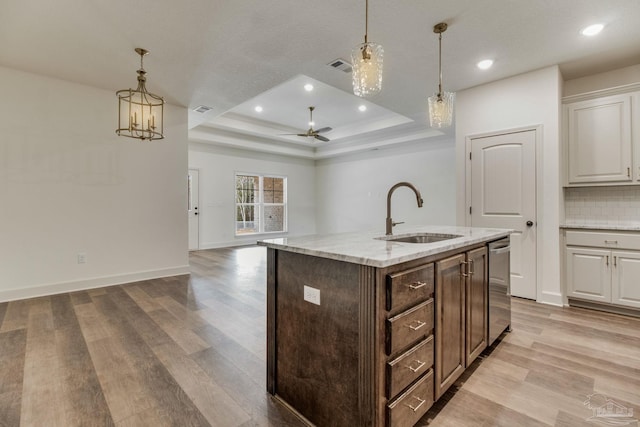 kitchen with a tray ceiling, backsplash, light wood-style floors, open floor plan, and a sink