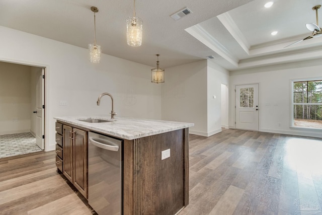 kitchen with a center island with sink, visible vents, a raised ceiling, light wood-style floors, and a sink