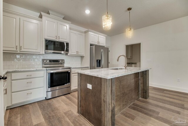 kitchen featuring light stone counters, stainless steel appliances, wood finished floors, a sink, and decorative backsplash