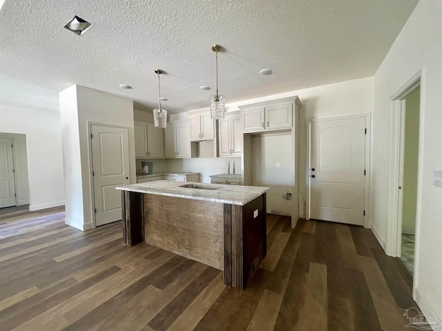 kitchen featuring dark wood-style floors, a center island, hanging light fixtures, a textured ceiling, and baseboards