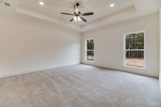 unfurnished room with a wealth of natural light, a tray ceiling, visible vents, and baseboards