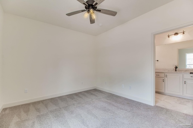 spare room featuring light carpet, ceiling fan, a sink, and baseboards