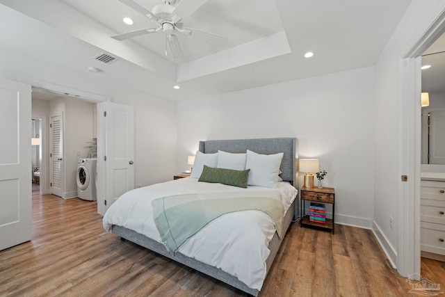 bedroom featuring recessed lighting, washer / clothes dryer, wood finished floors, baseboards, and a tray ceiling