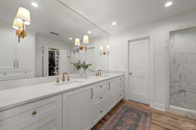 bathroom featuring a tile shower, wood finished floors, a sink, and visible vents