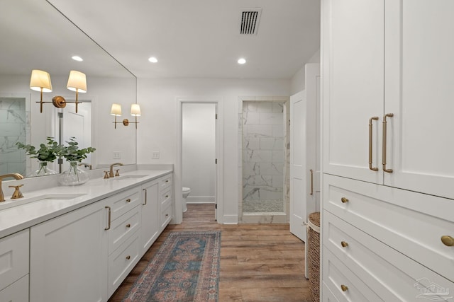 bathroom with visible vents, a sink, a marble finish shower, and wood finished floors