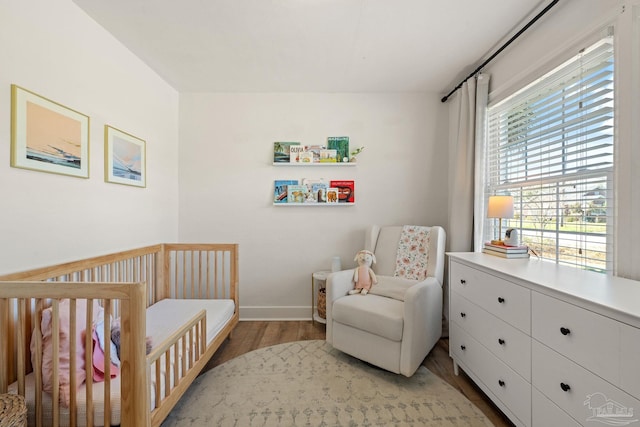 bedroom with light wood finished floors, a crib, and baseboards