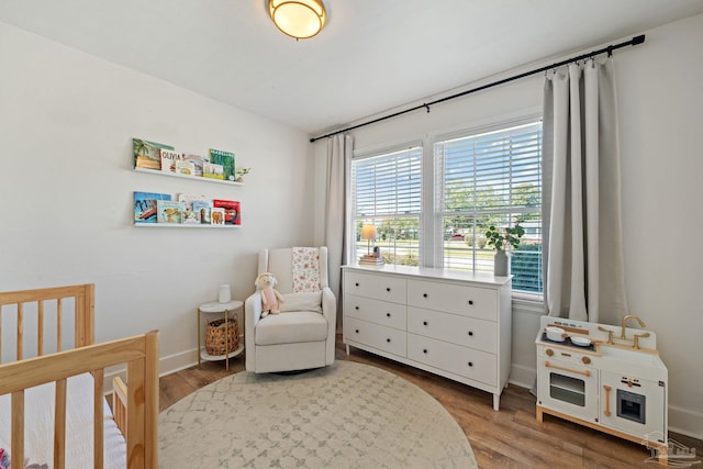 bedroom featuring a crib, wood finished floors, and baseboards