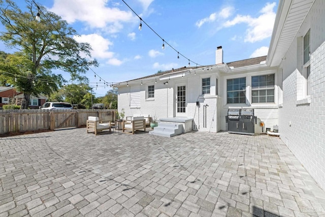 rear view of house featuring brick siding, a chimney, outdoor lounge area, a patio area, and fence