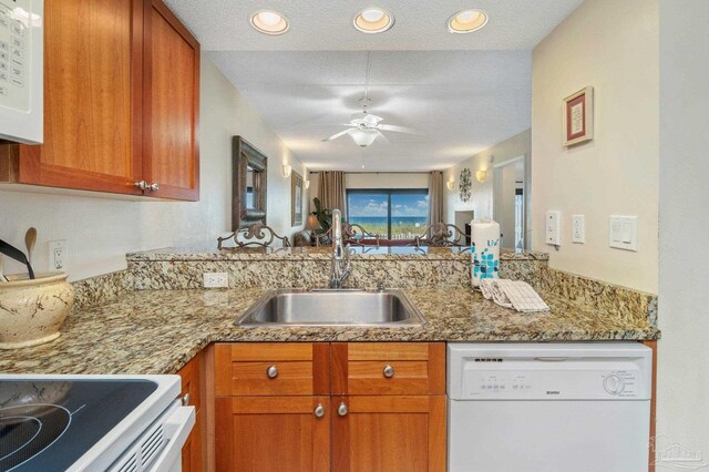 kitchen featuring white appliances, sink, light stone counters, a textured ceiling, and ceiling fan