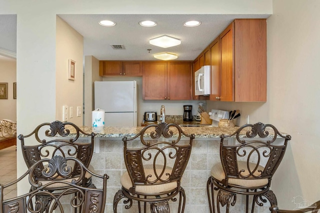 kitchen with light tile patterned floors, white appliances, light stone countertops, and brown cabinets