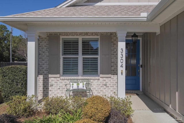 doorway to property with brick siding, board and batten siding, and a shingled roof