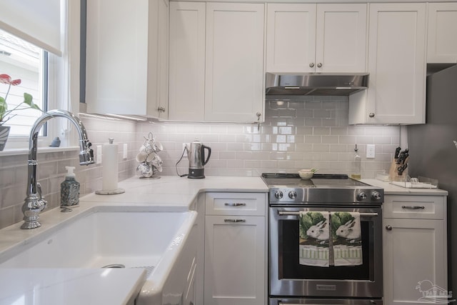 kitchen featuring white cabinets, light stone counters, stainless steel range with electric cooktop, under cabinet range hood, and a sink