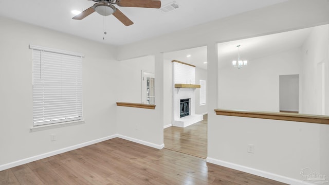 unfurnished living room with a fireplace, ceiling fan with notable chandelier, and hardwood / wood-style flooring