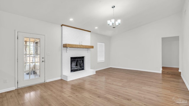 unfurnished living room featuring a notable chandelier, vaulted ceiling, light wood-type flooring, and a brick fireplace