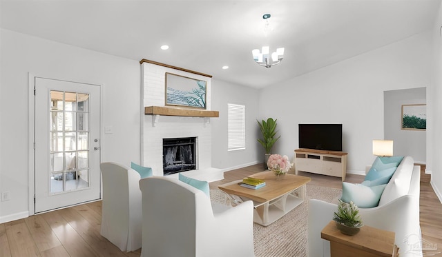 living room featuring a brick fireplace, a chandelier, and light hardwood / wood-style flooring