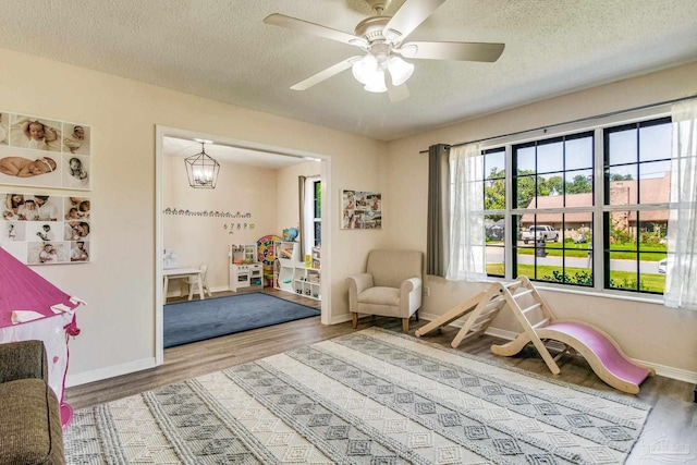 game room featuring ceiling fan with notable chandelier, hardwood / wood-style flooring, and a textured ceiling