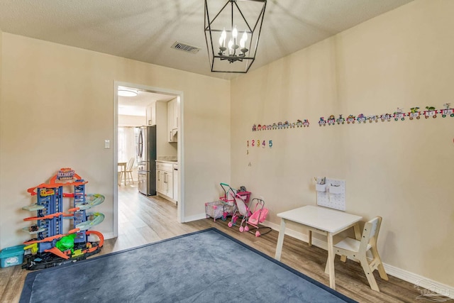 playroom with a notable chandelier, light wood-type flooring, and a textured ceiling