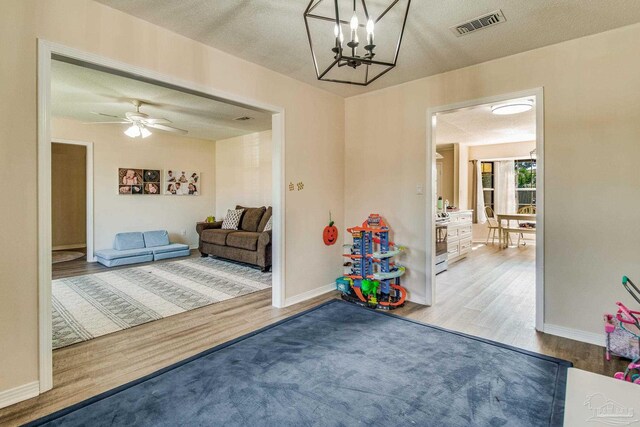 recreation room with ceiling fan with notable chandelier, wood-type flooring, and a textured ceiling