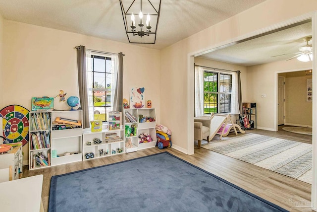 recreation room with ceiling fan with notable chandelier, hardwood / wood-style floors, and a textured ceiling