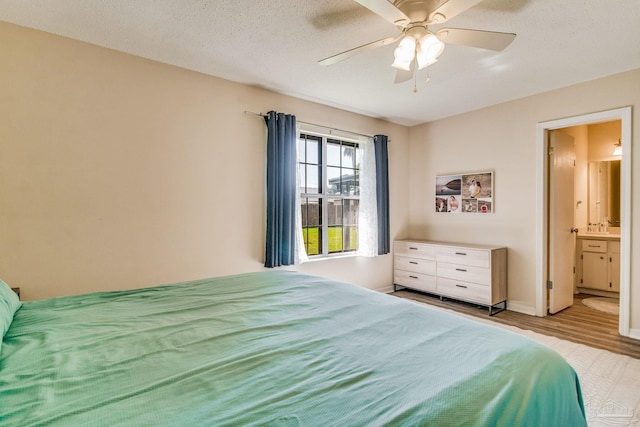 bedroom with ceiling fan, a textured ceiling, connected bathroom, and light hardwood / wood-style floors