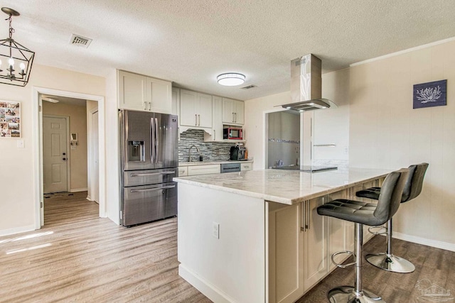 kitchen featuring light stone counters, hanging light fixtures, exhaust hood, stainless steel refrigerator with ice dispenser, and built in microwave