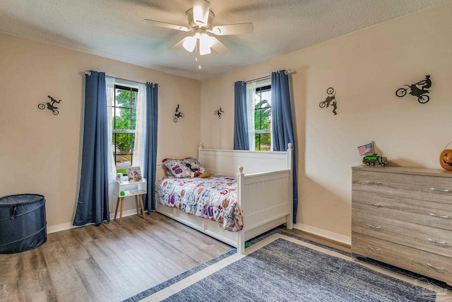 bedroom with hardwood / wood-style flooring, multiple windows, ceiling fan, and a textured ceiling