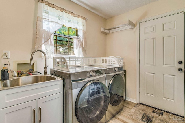 clothes washing area featuring sink, a textured ceiling, light hardwood / wood-style flooring, cabinets, and washer and dryer